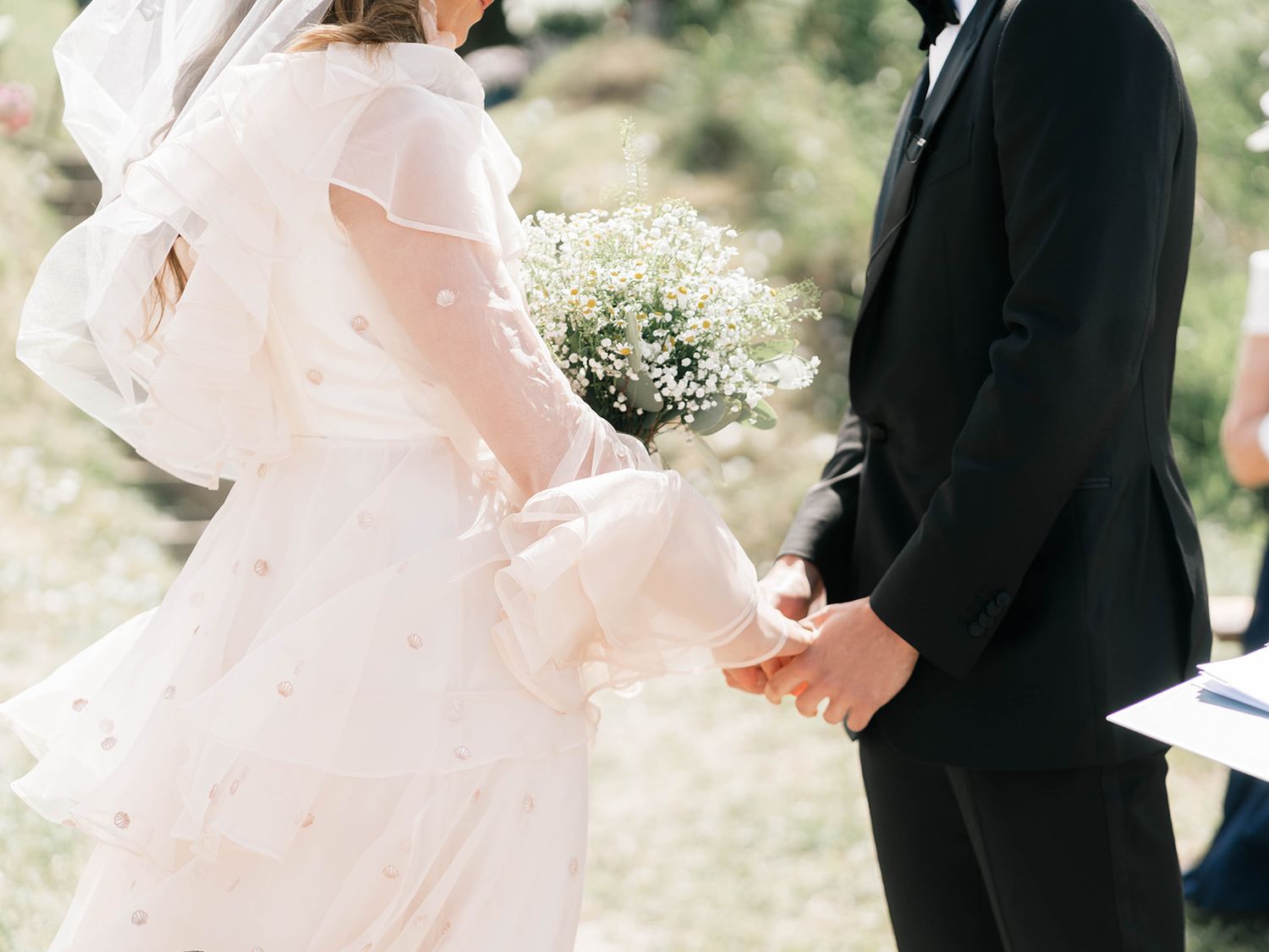 A couple exchanges rings during an outdoor wedding ceremony surrounded by greenery.