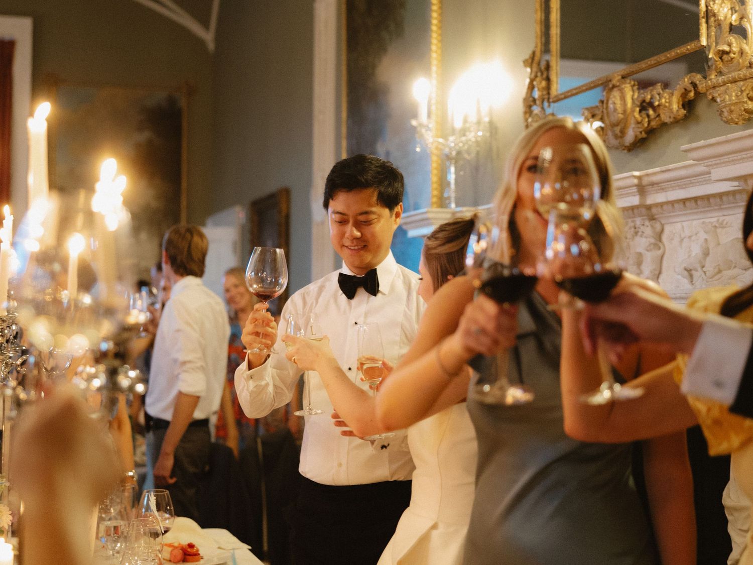 Wedding reception guests raising wine glasses during an elegant candlelit dinner celebration.