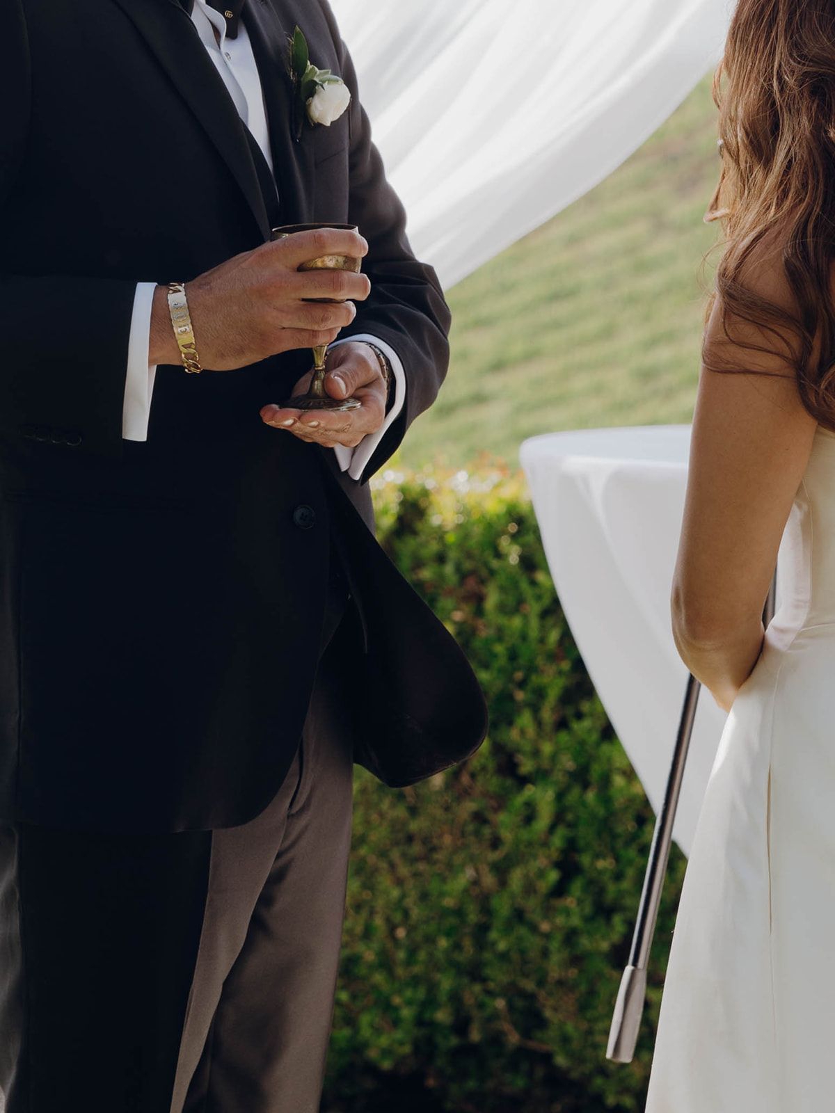Close-up view of formal wedding attire with a glass of champagne during an outdoor ceremony.