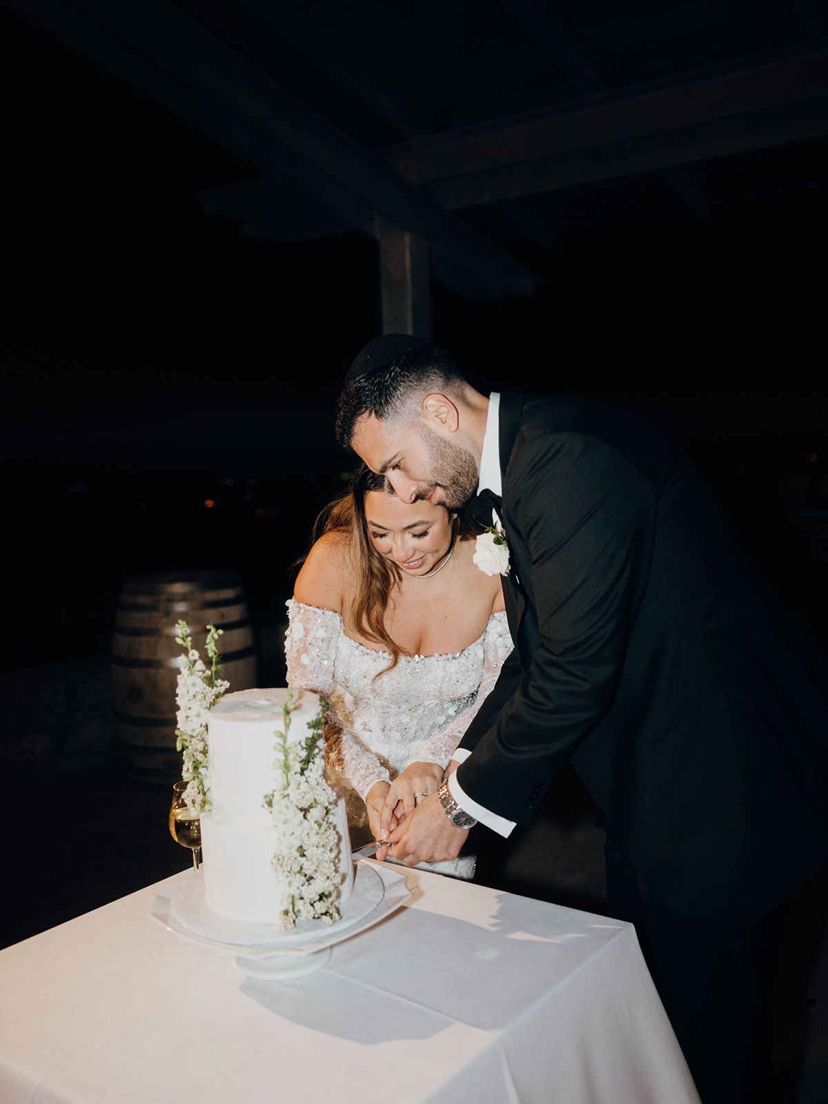 A newlywed couple cuts their elegant white wedding cake decorated with floral details.