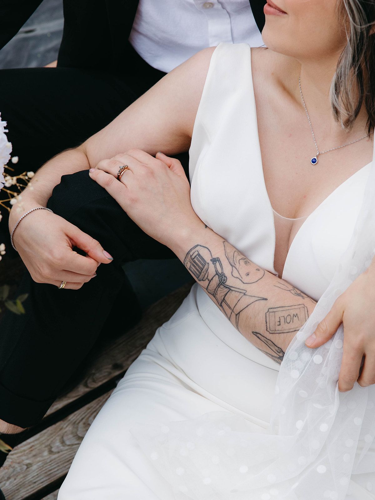 Close-up of newlyweds showing elegant white wedding dress and detailed arm tattoo sleeve in intimate moment.