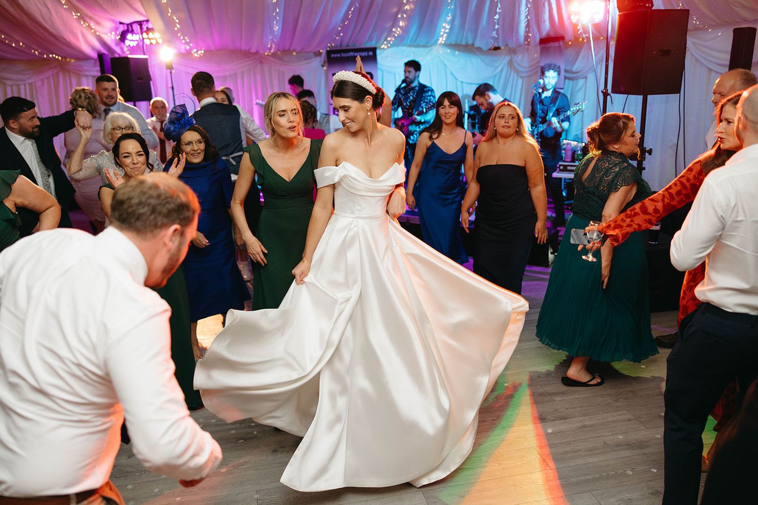 A large wedding reception dance party in an illuminated tent with people dancing and celebrating on the dance floor.