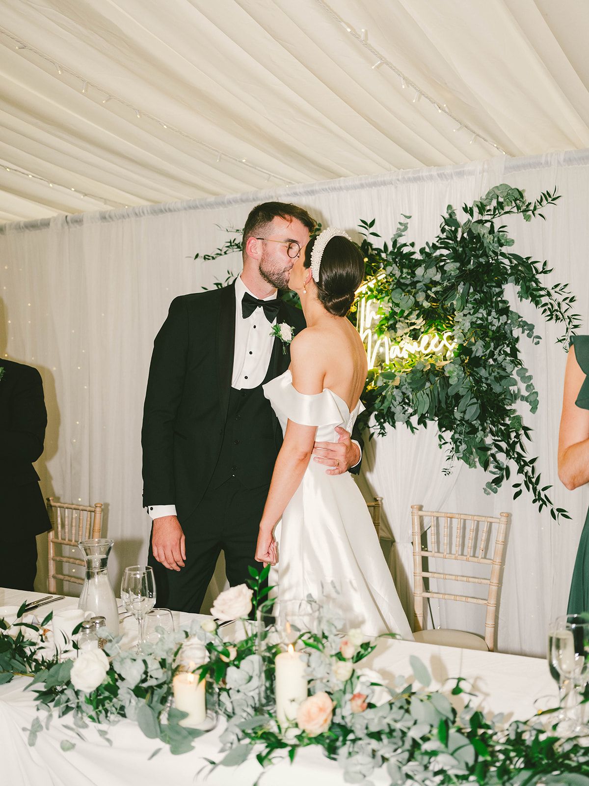 Elegant wedding reception in white tent with greenery decor and romantic candlelight on dining table.