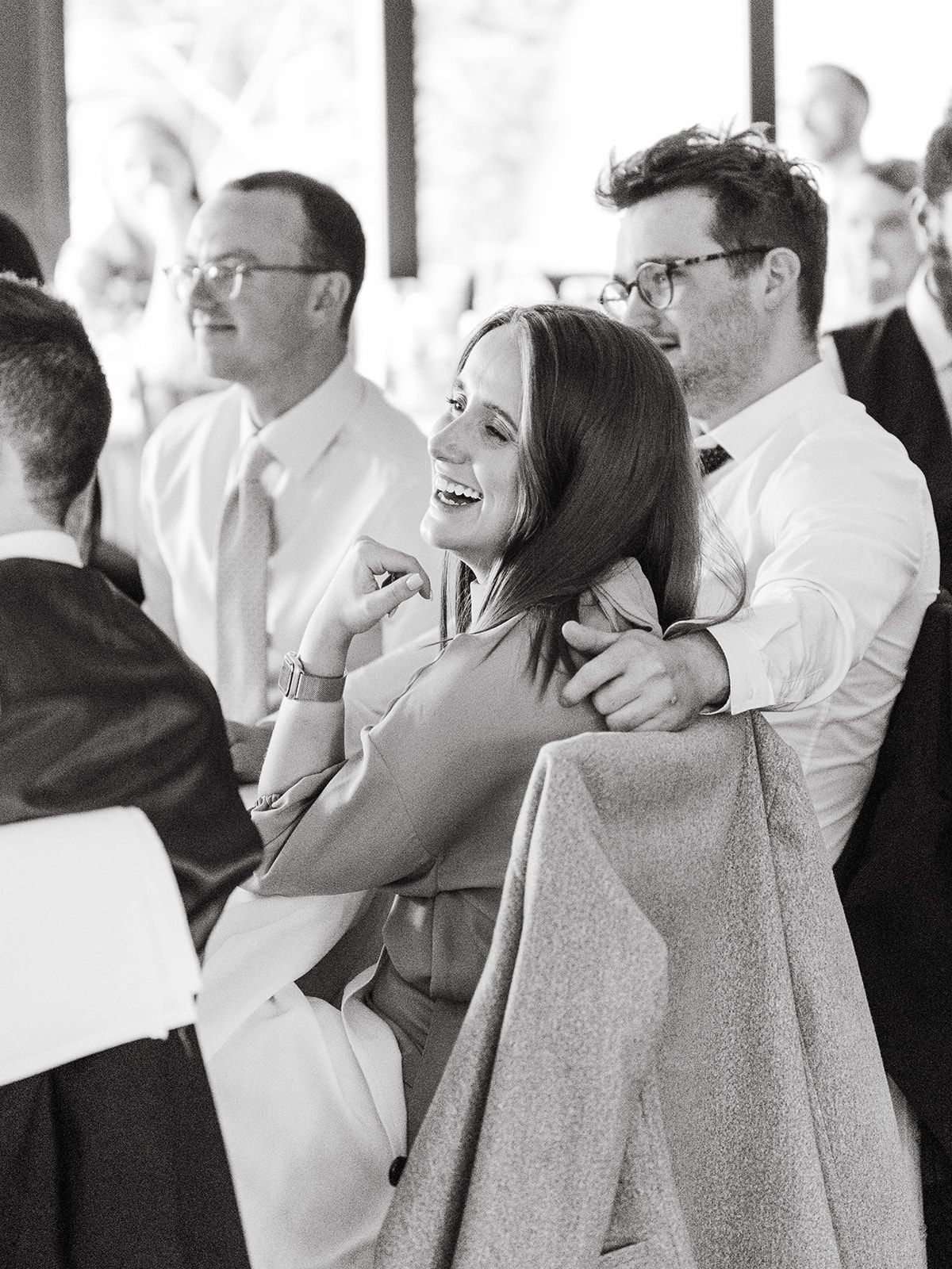A candid black and white photo at a gathering shows people laughing together in formal attire.