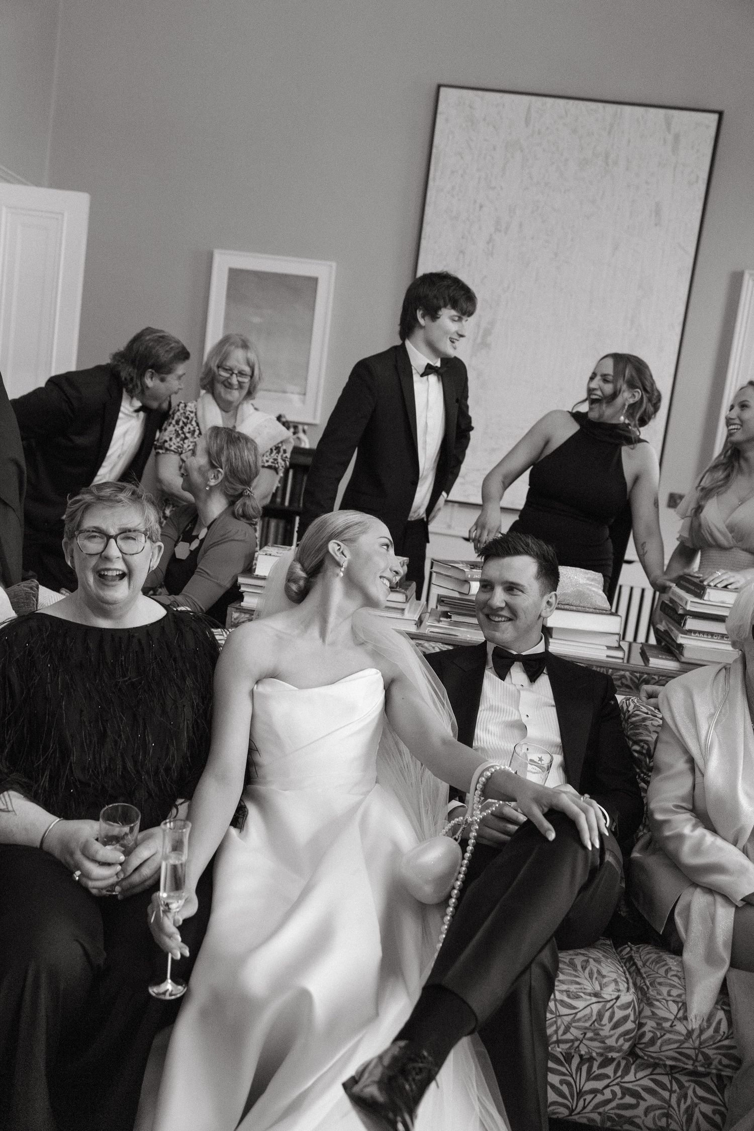 Black and white photo of bride and groom laughing with wedding guests in an elegant room.