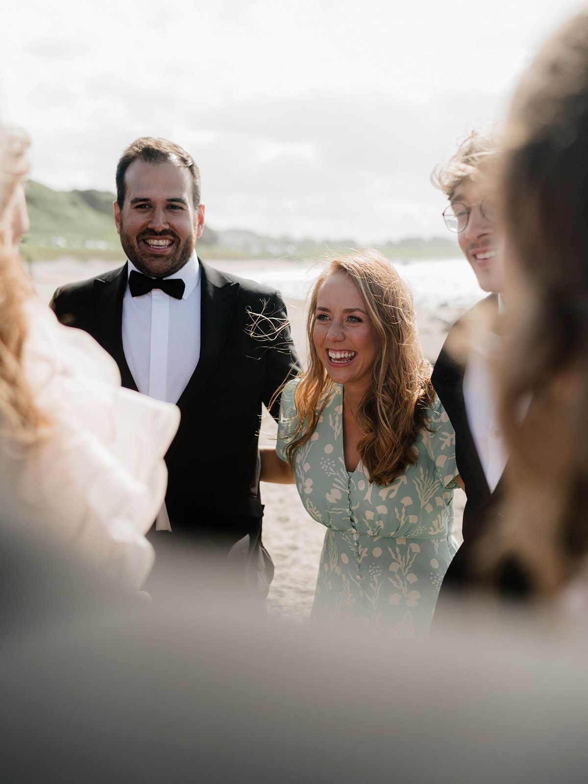 Candid wedding reception photo showing guests laughing together on beach.