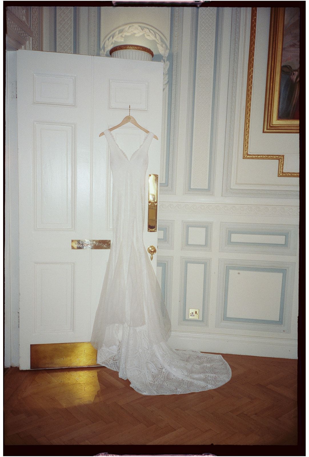 A white wedding dress hangs elegantly on display in a classic room with white paneled walls.