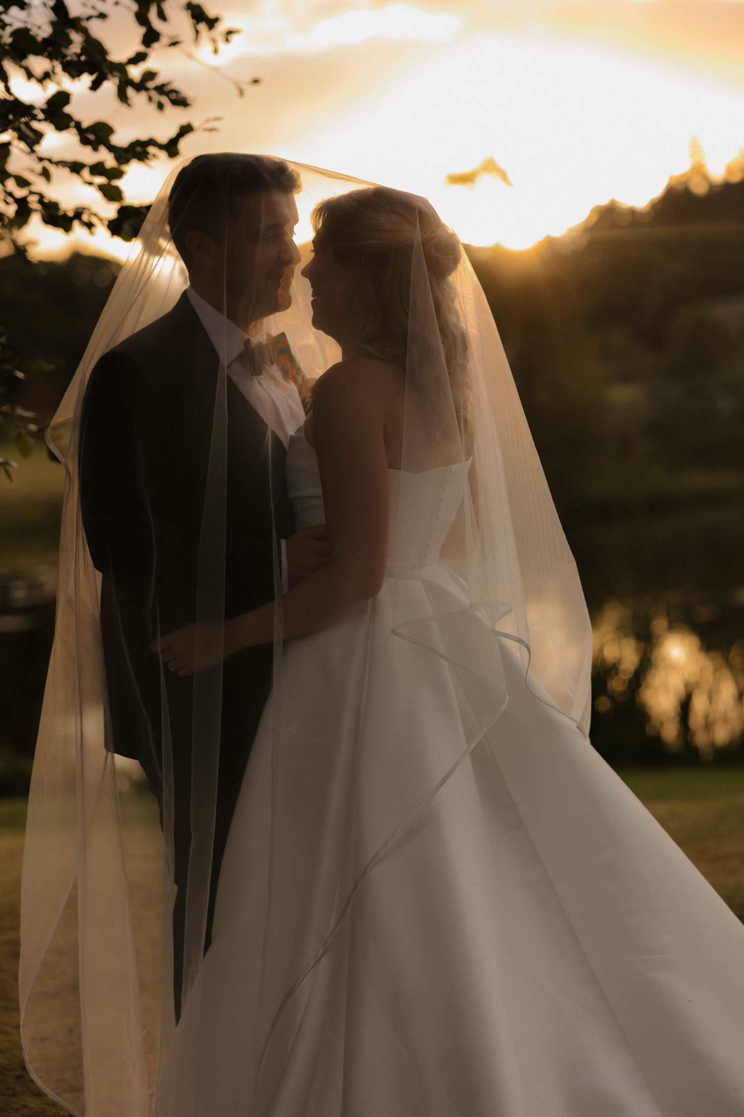 Romantic silhouette of newlyweds against sunset with flowing veil.