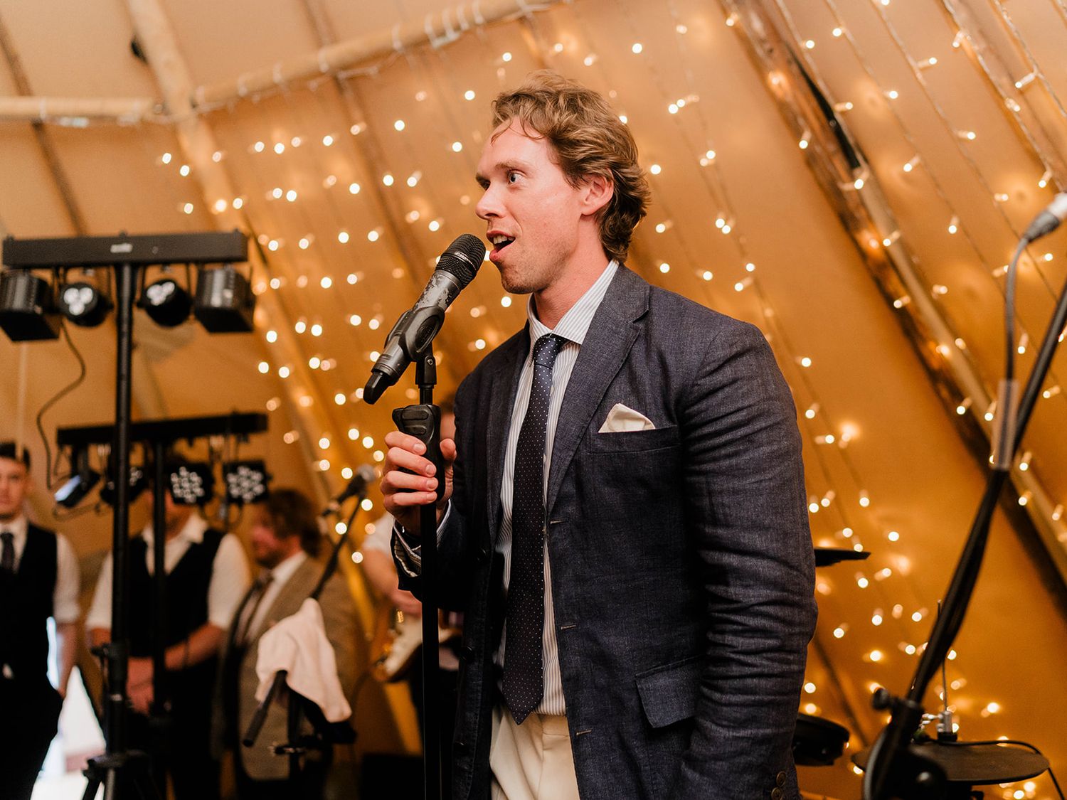 Singer performing at a wedding reception under warm string lights in a tent venue.