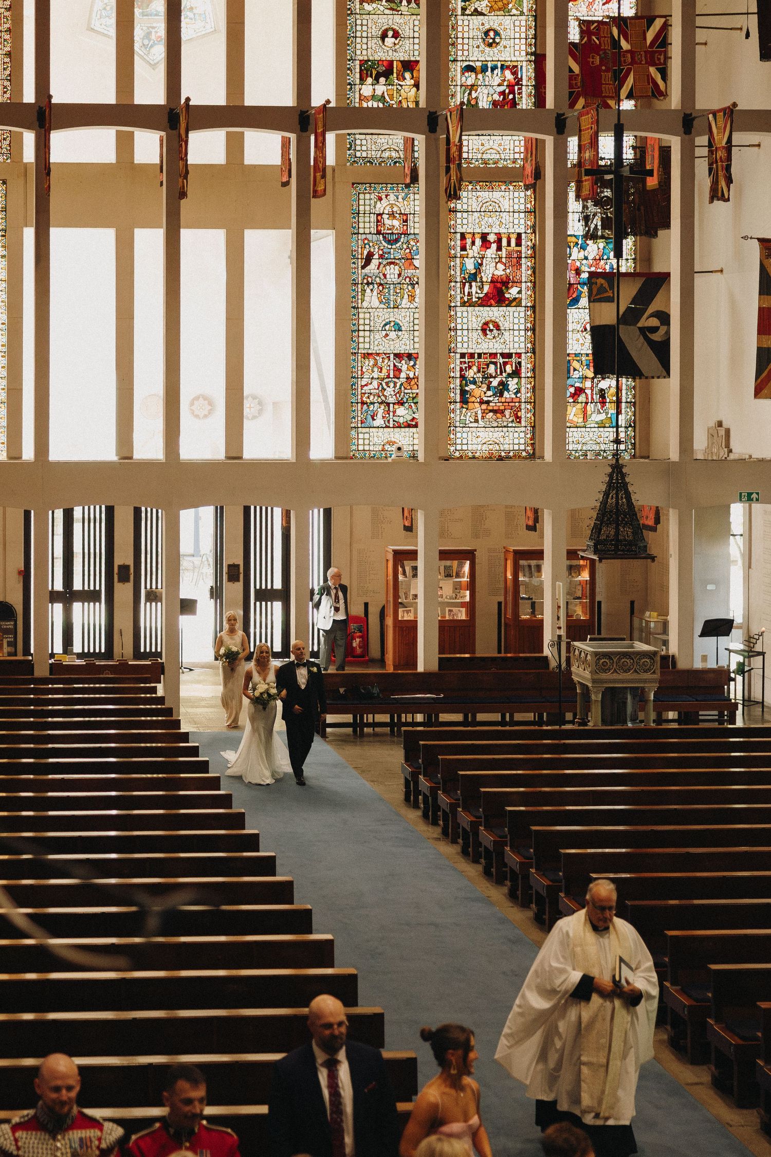 Interior view of a modern church with rows of wooden pews and stained glass windows along the walls.