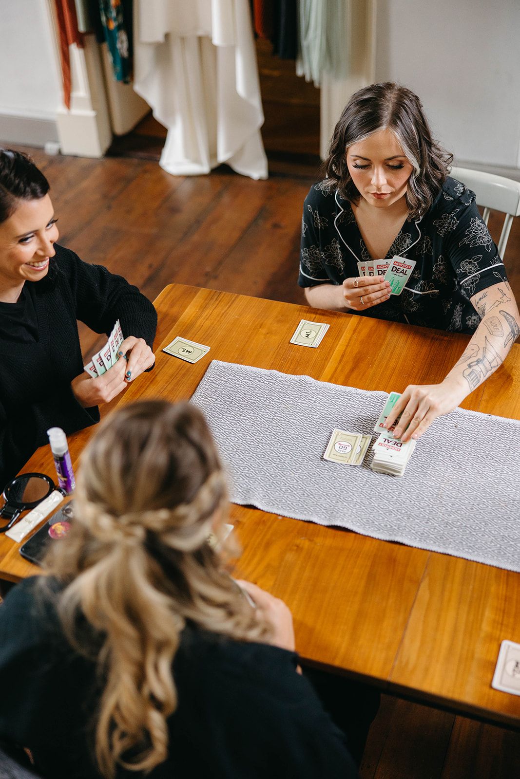 Friends playing a card game together at wooden table with grey placemat on hardwood floor.