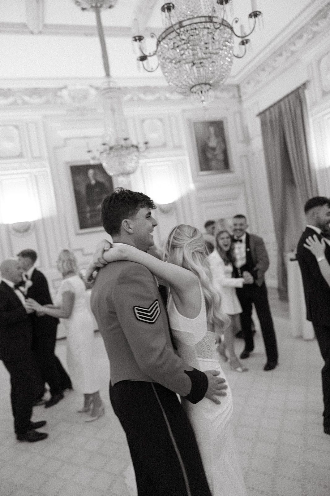 Couples dancing together in an elegant white ballroom with crystal chandeliers during a formal event.