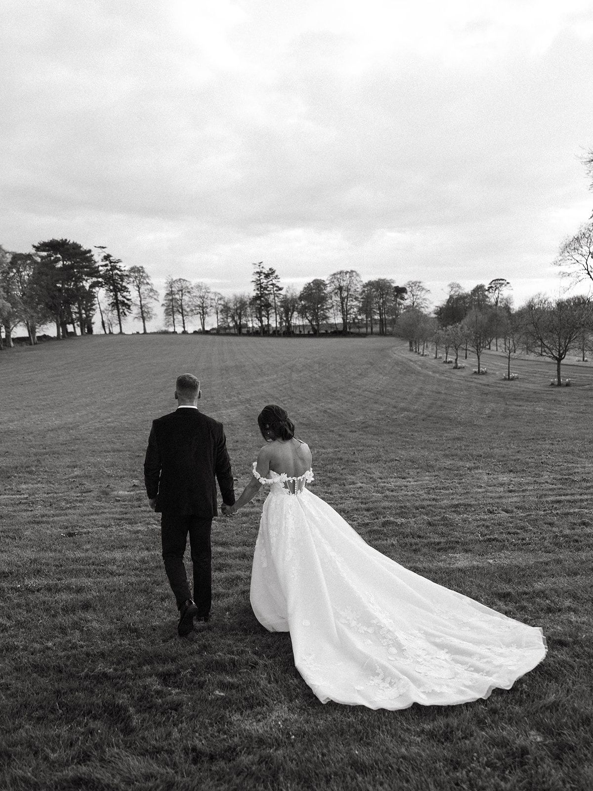 A black and white wedding portrait of a couple walking through a scenic hillside field.