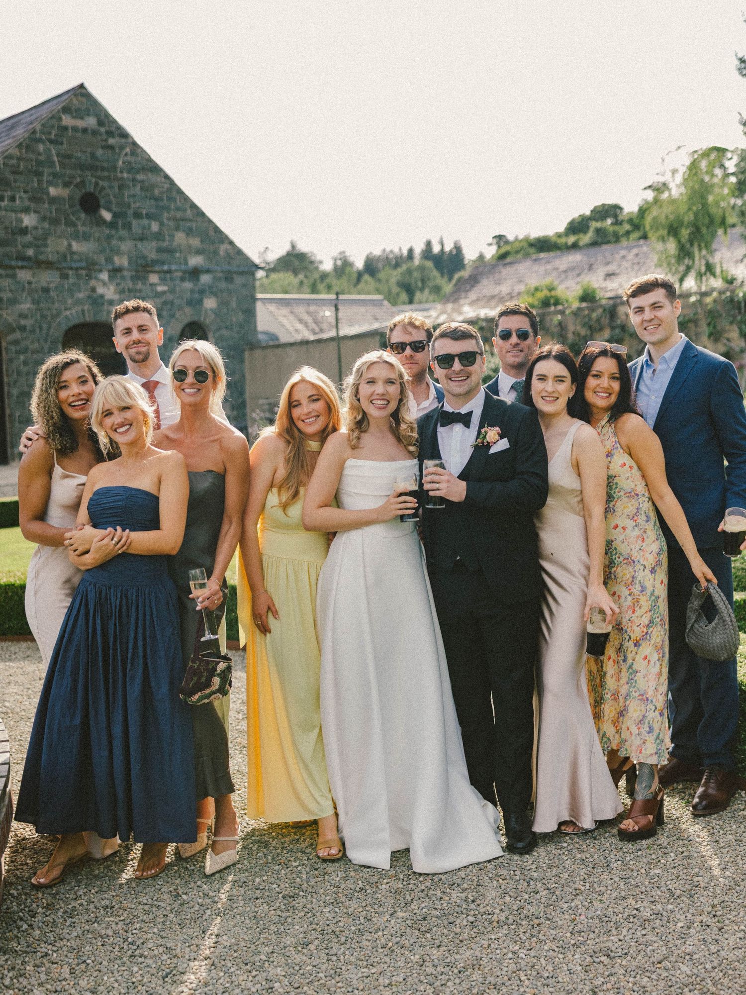 Wedding party group photo with guests in navy and yellow dresses posing outside a stone building.