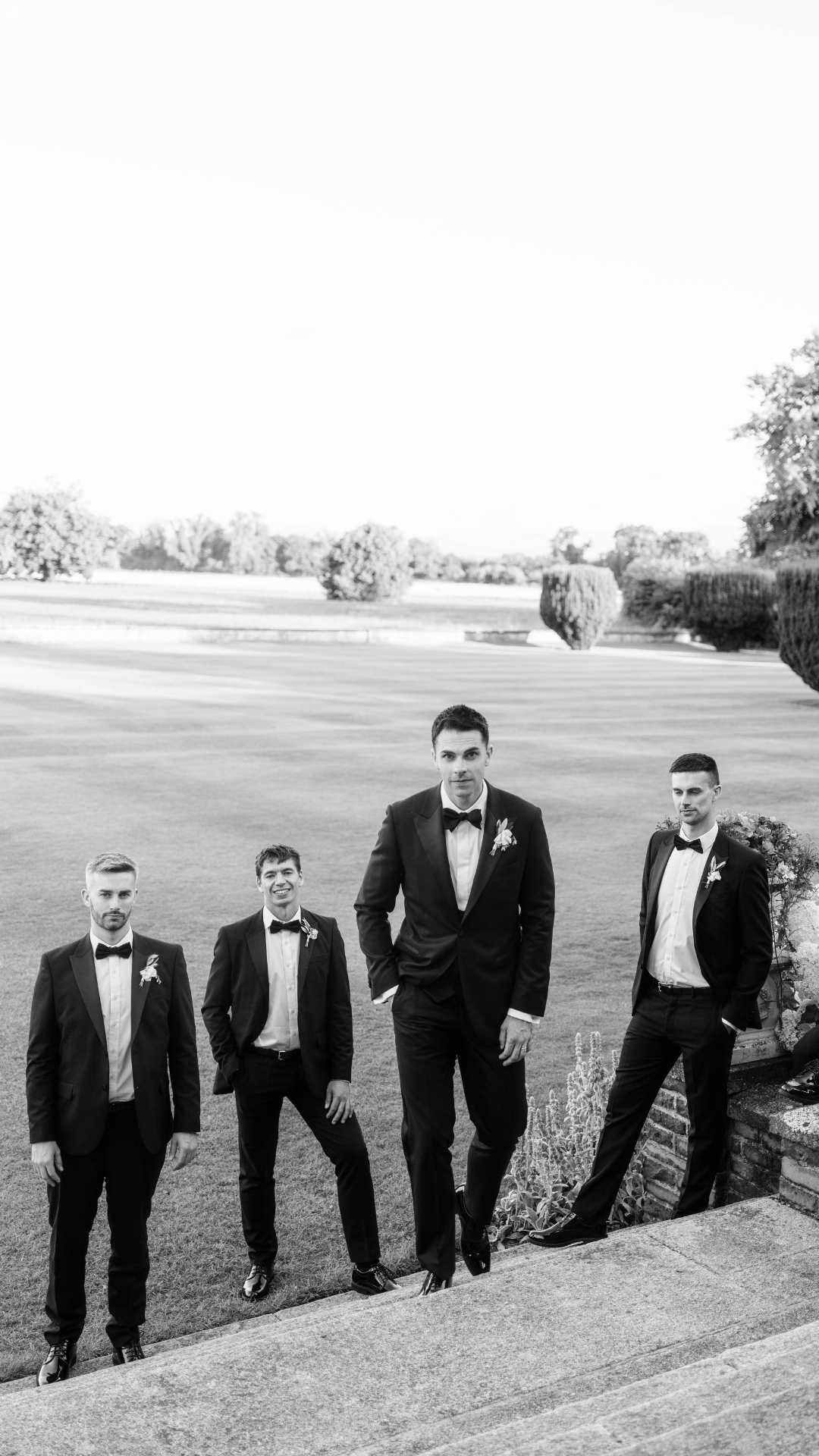 Groomsmen in black tuxedos posing on steps of a golf course.