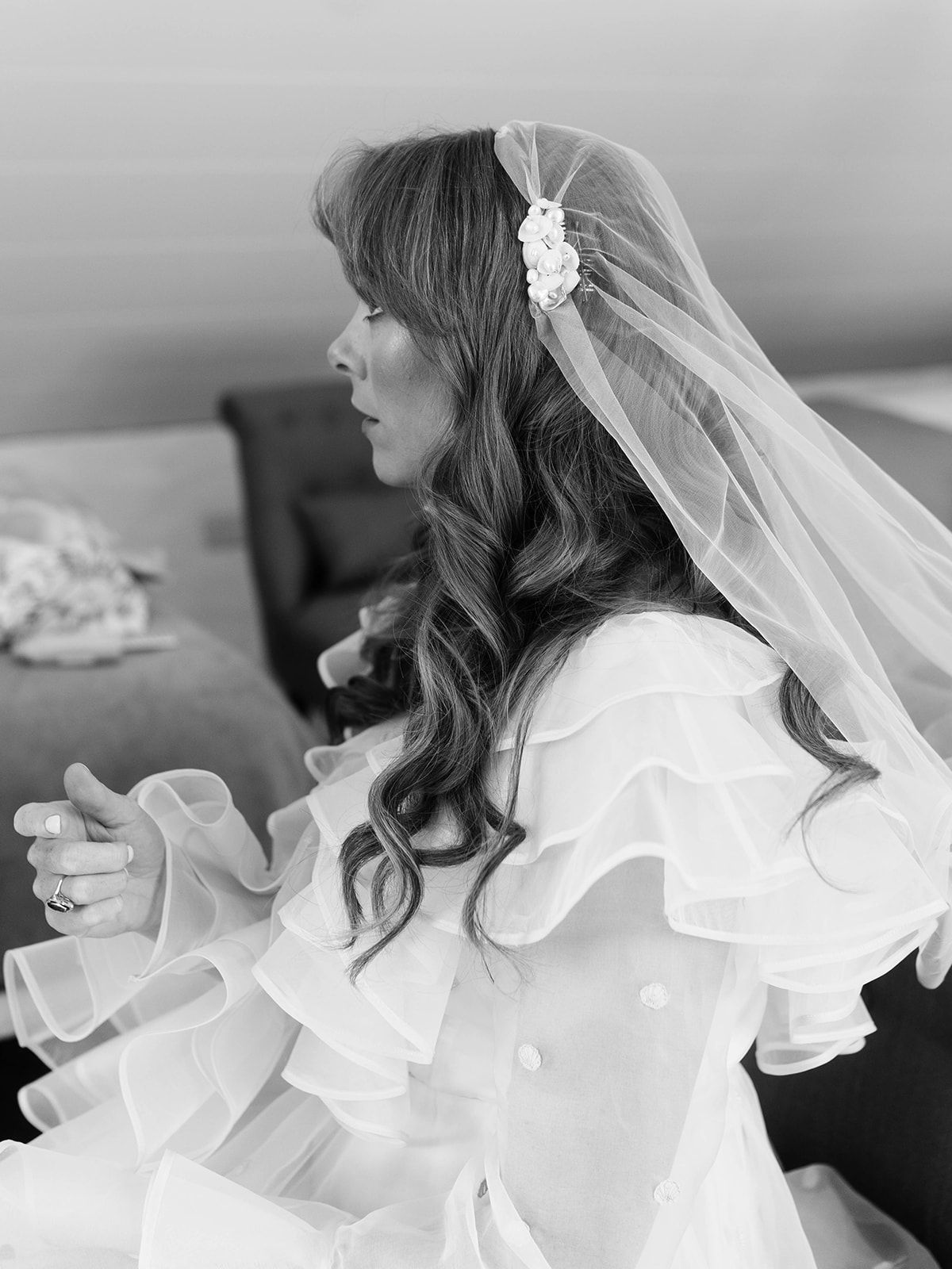 Black and white profile shot of bride in ruffled dress with veil and flowing curls.