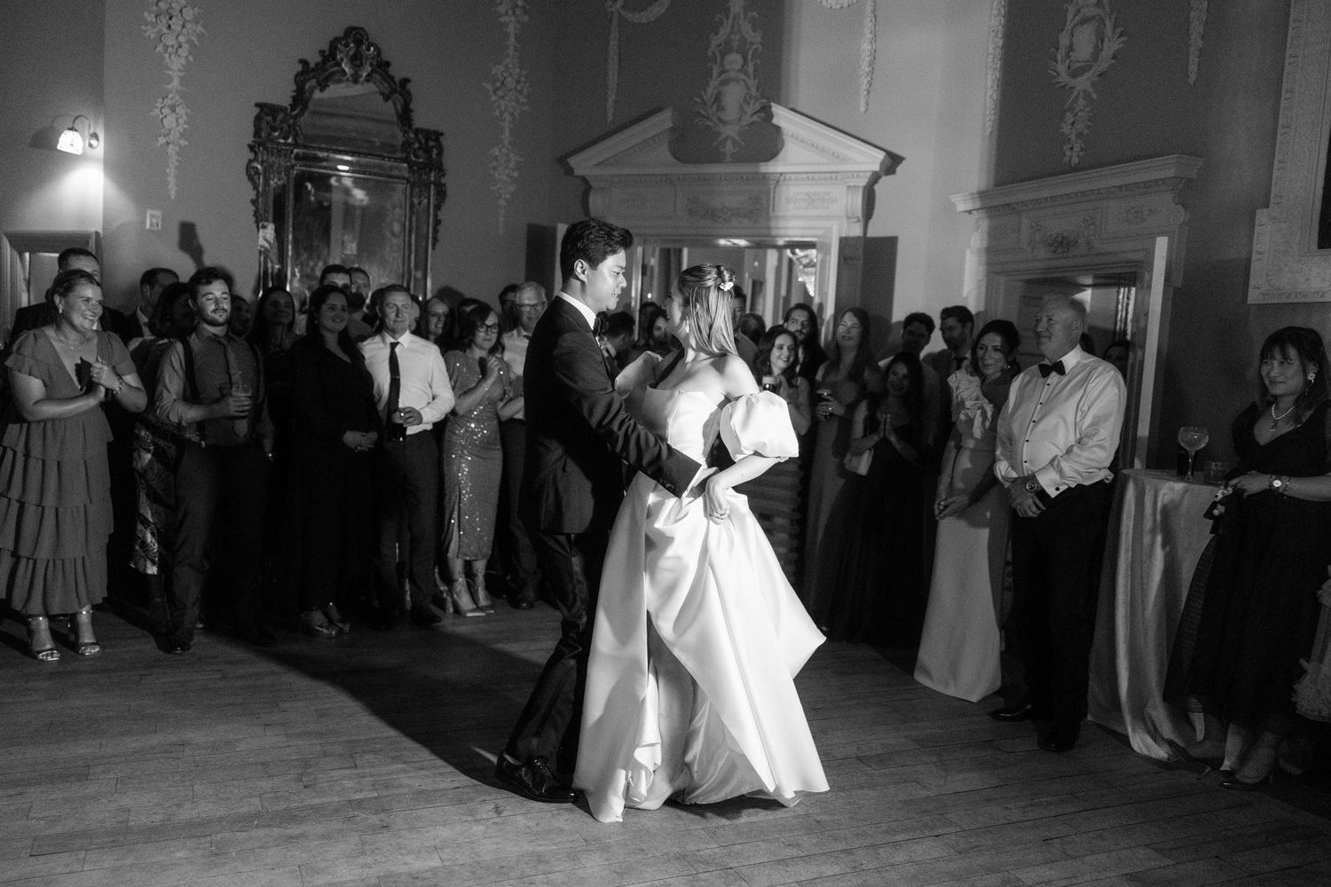 First dance at a wedding reception captured in black and white with guests watching.