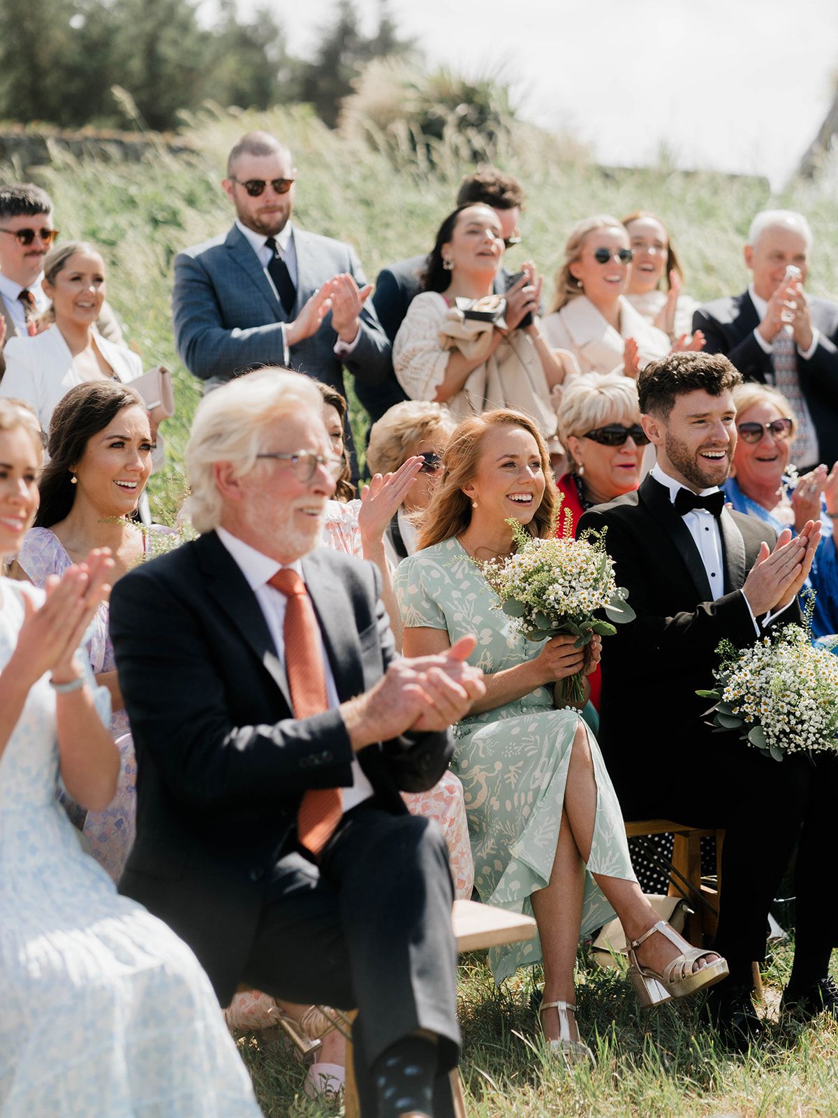 Wedding guests applaud during an outdoor ceremony with baby's breath bouquets.