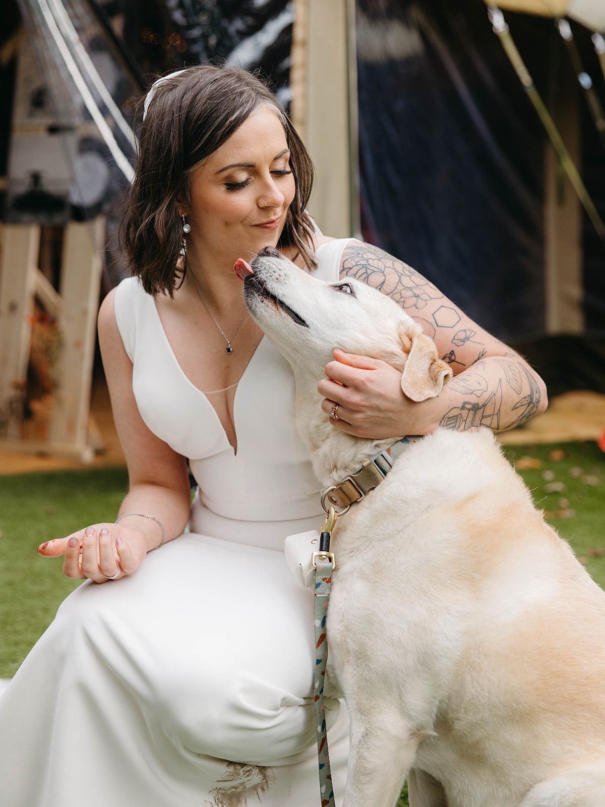 A sweet moment between a white dog and someone in a wedding dress outdoors.
