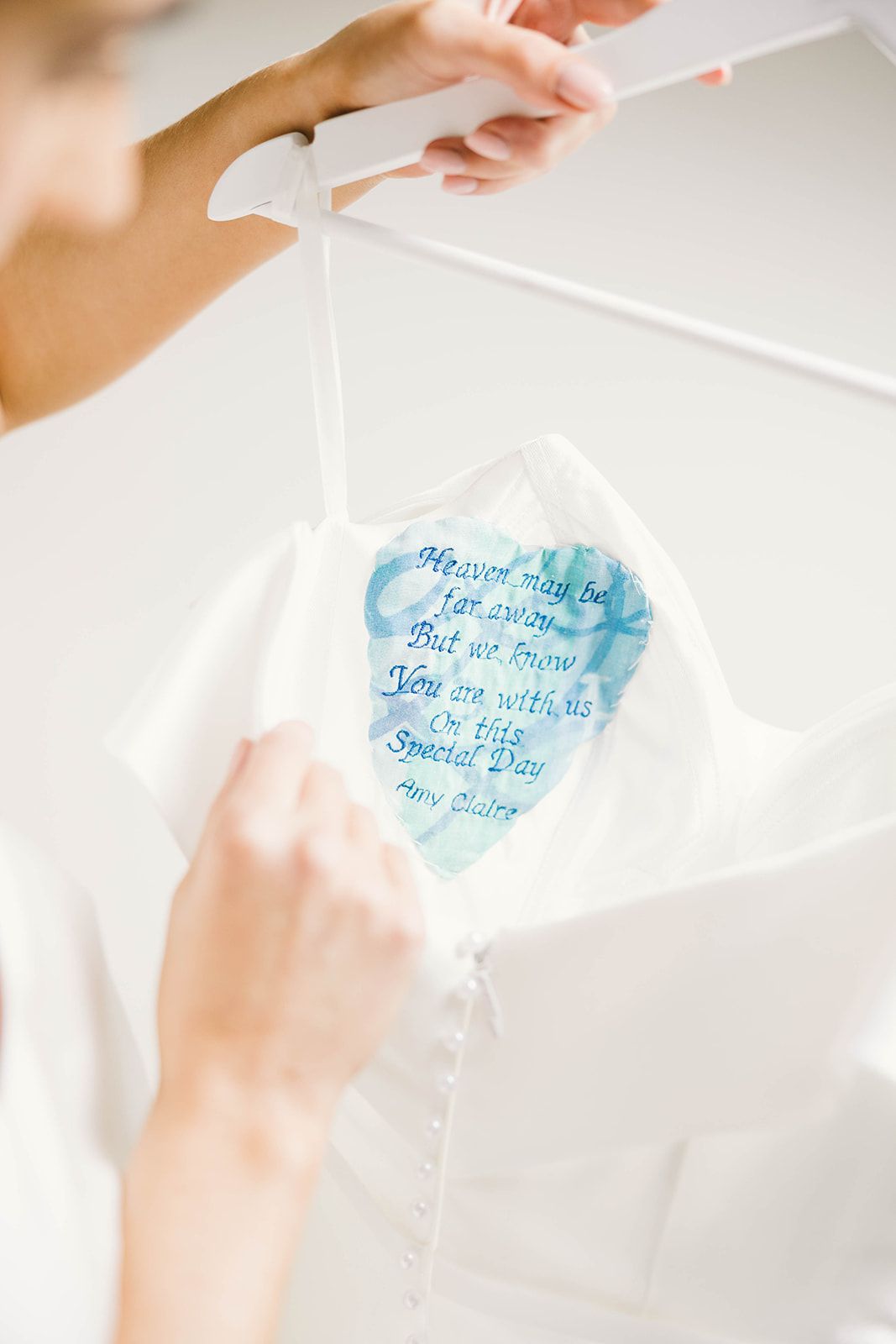 Hands hold a delicate white handkerchief with blue watercolor text in a heart shape.