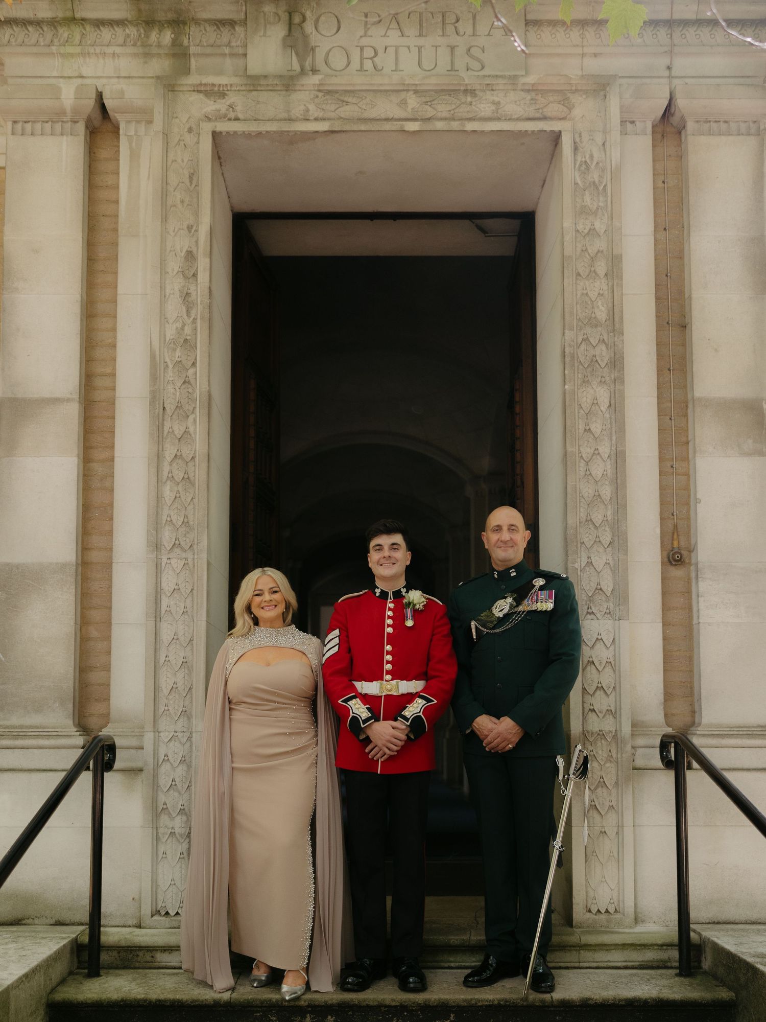 Military service members and dignitaries stand in formal dress at a memorial ceremony entrance.