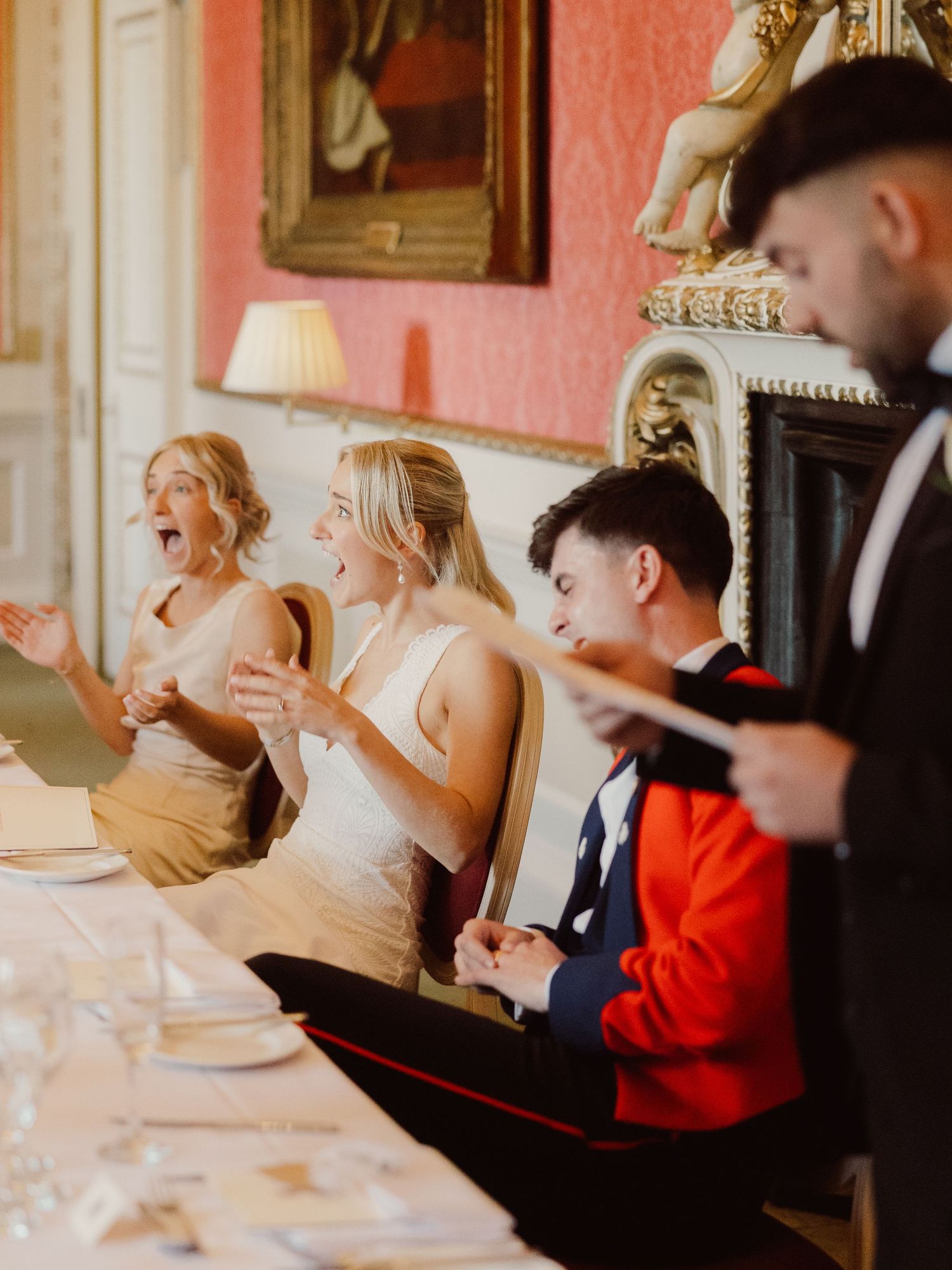 Wedding guests enjoying a formal dinner reception at an elegant venue with pink walls and ornate decor.