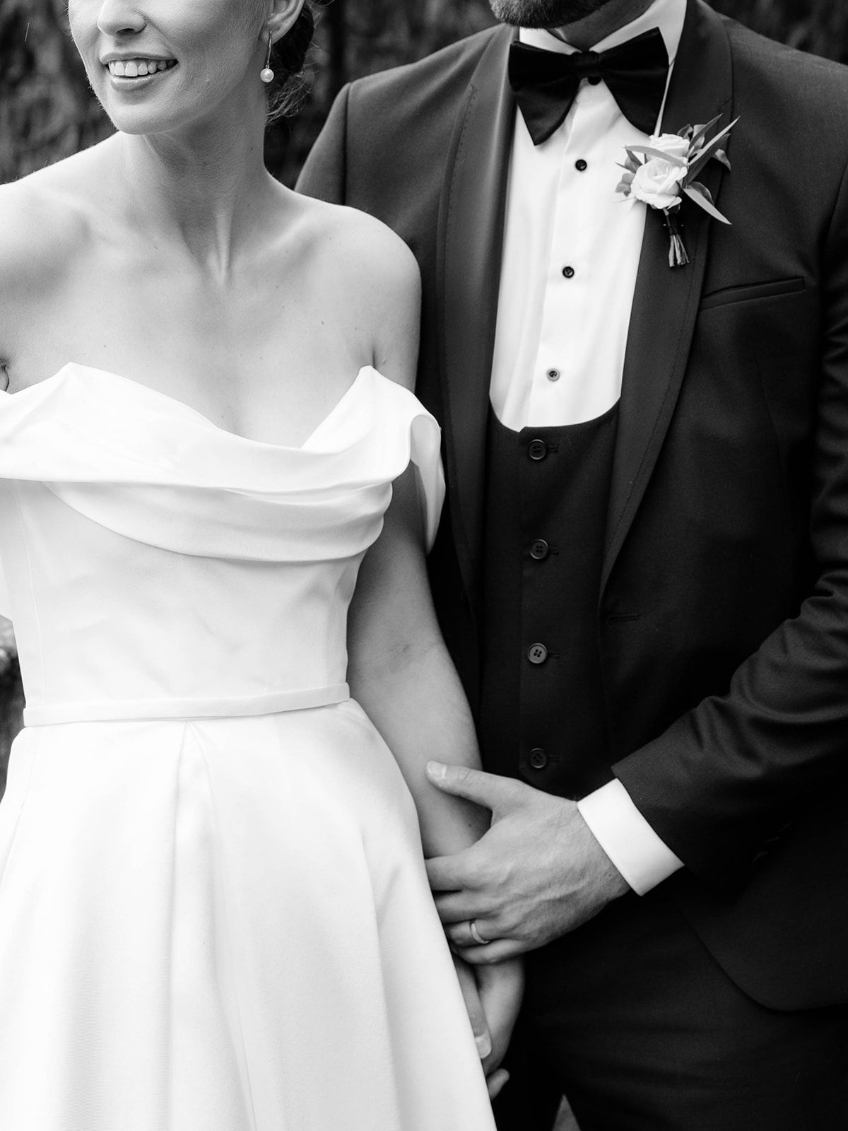 Close-up black and white photo of a wedding couple in classic attire showing off-shoulder bridal gown and groom's tuxedo.