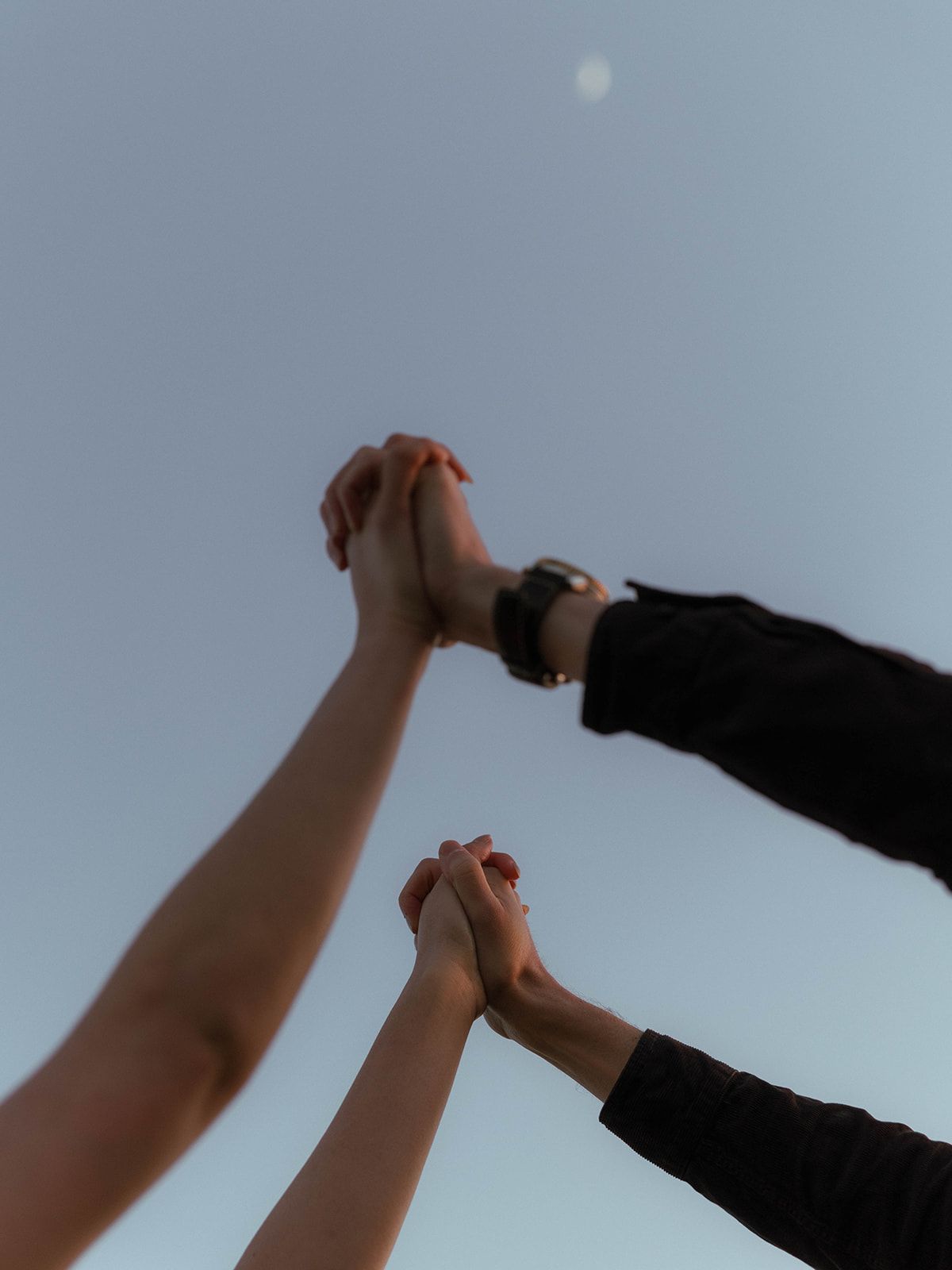 A sequence of hands reaching up to pour wine from a dark bottle against a light blue sky background.