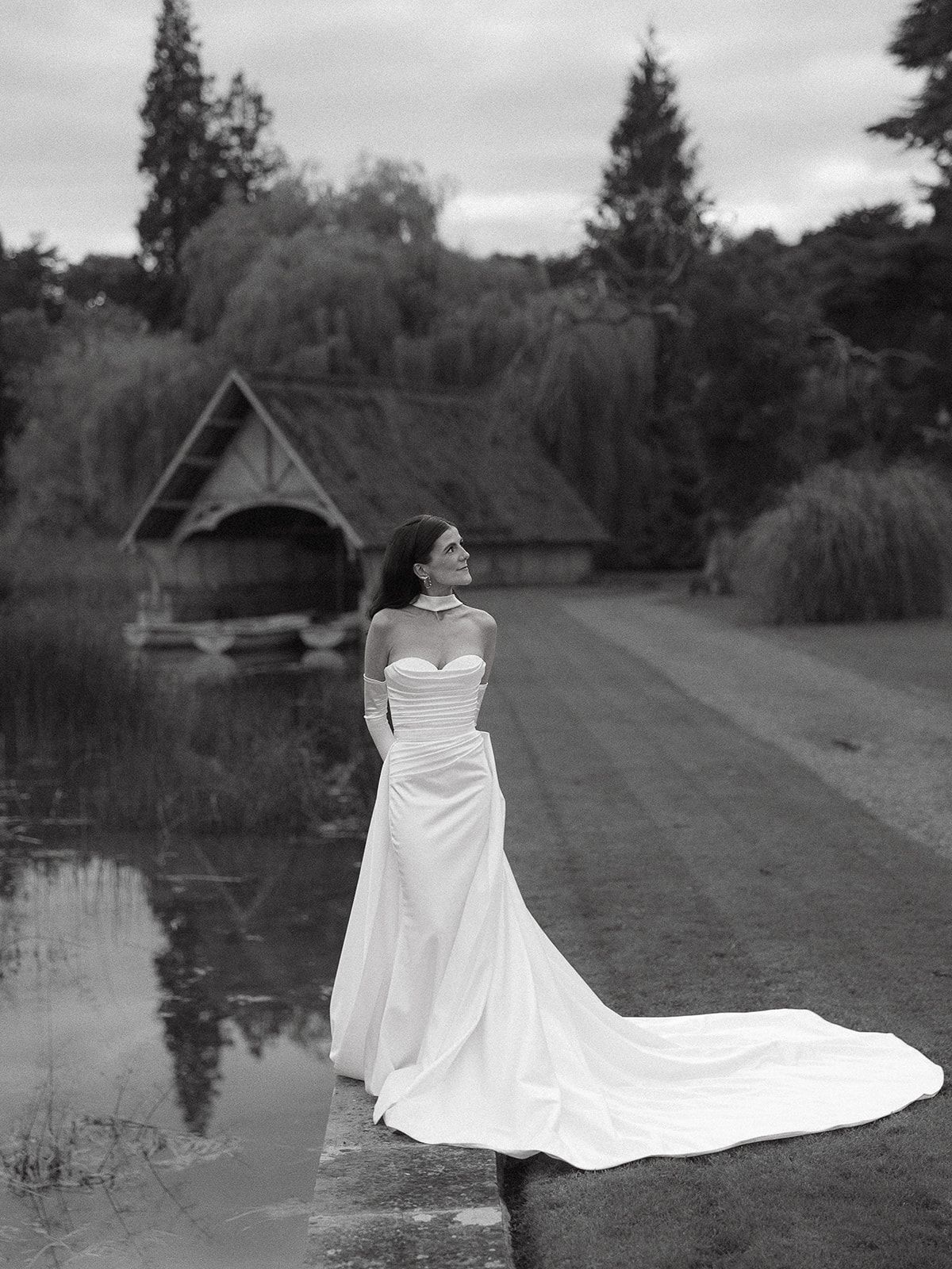 A series of black and white photos showing a bride in a flowing white wedding dress near a reflective pond at dusk.
