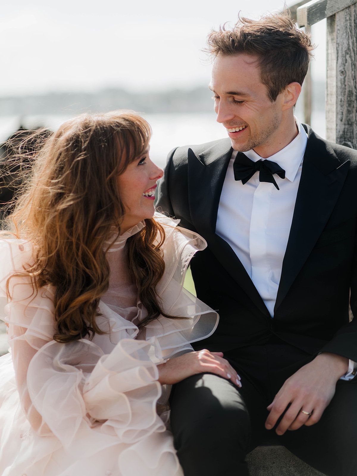 Candid moment of newlyweds sharing laughter against coastal backdrop.