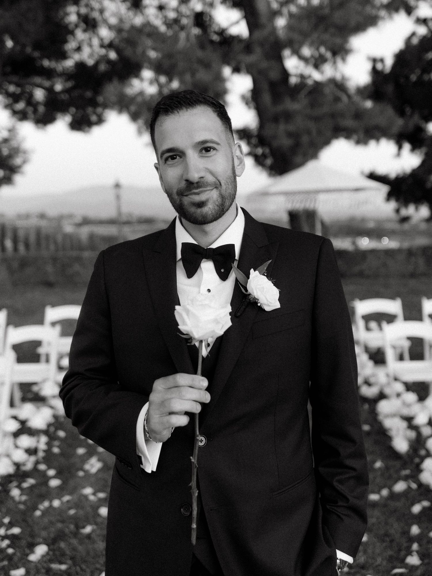 Three black and white photos of a groom in a tuxedo and bowtie enjoying champagne at an outdoor wedding reception.