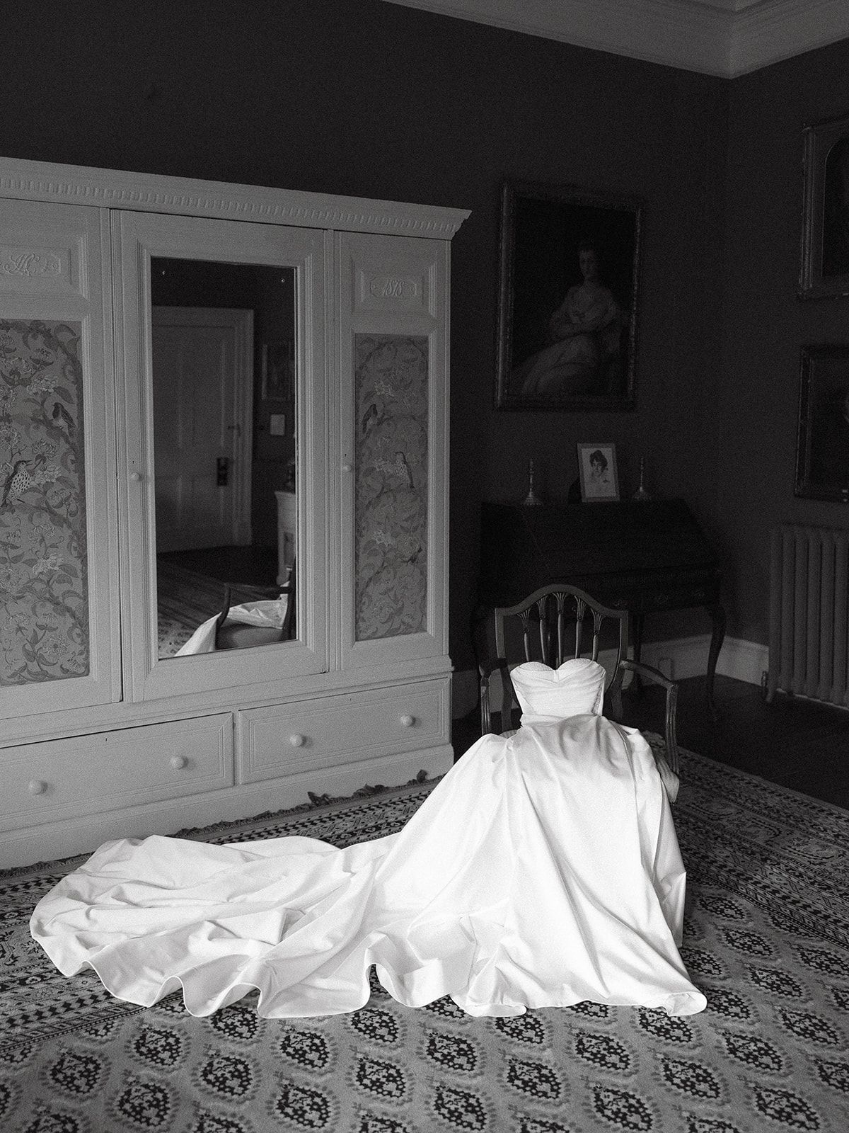 A white sheet ghost figure sits on patterned carpet in a dimly lit room with white furniture and wall art.