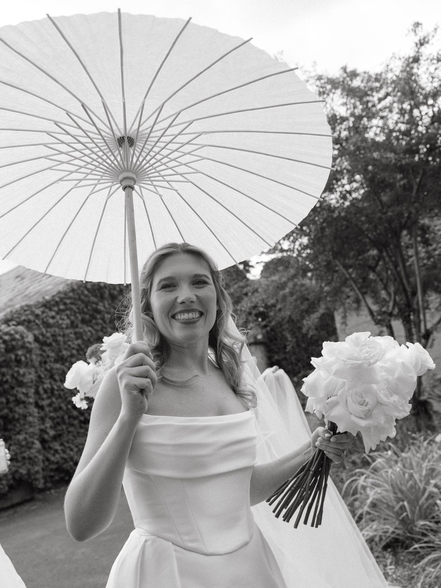 Joyful wedding portraits with a white parasol in an outdoor garden setting.