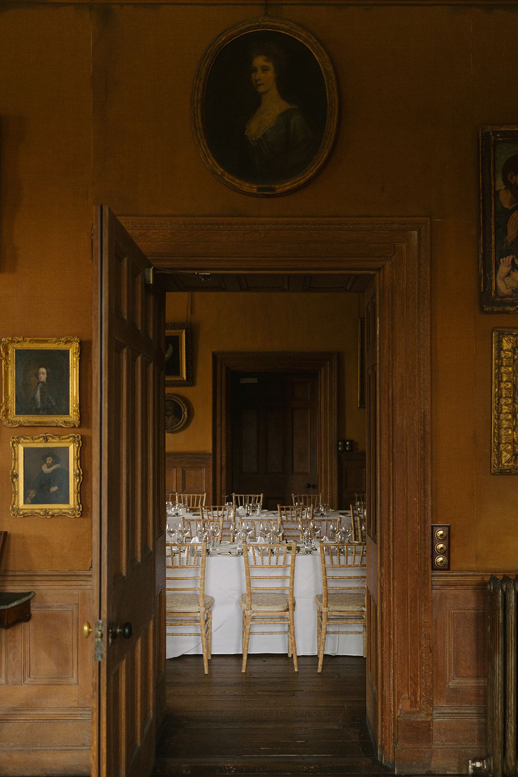 Historic wood-paneled room with portrait paintings and empty chairs lined up for an elegant event.