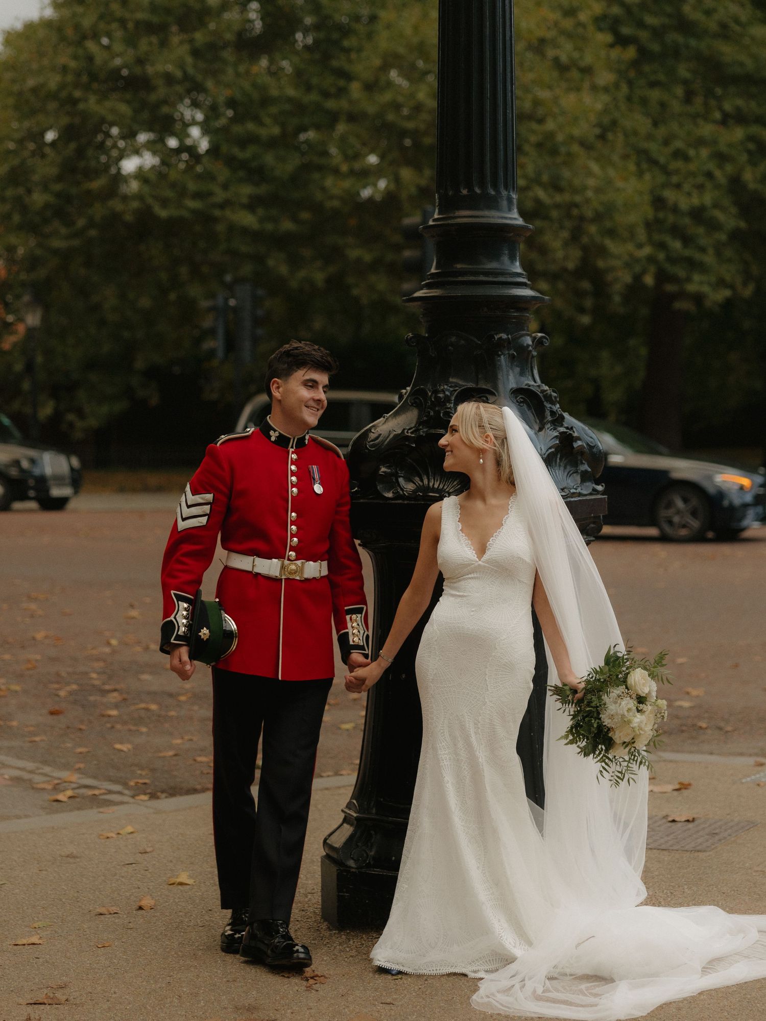 A wedding couple poses in iconic locations at London's Horse Guards Parade with elegant white dress and ceremonial red uniform.
