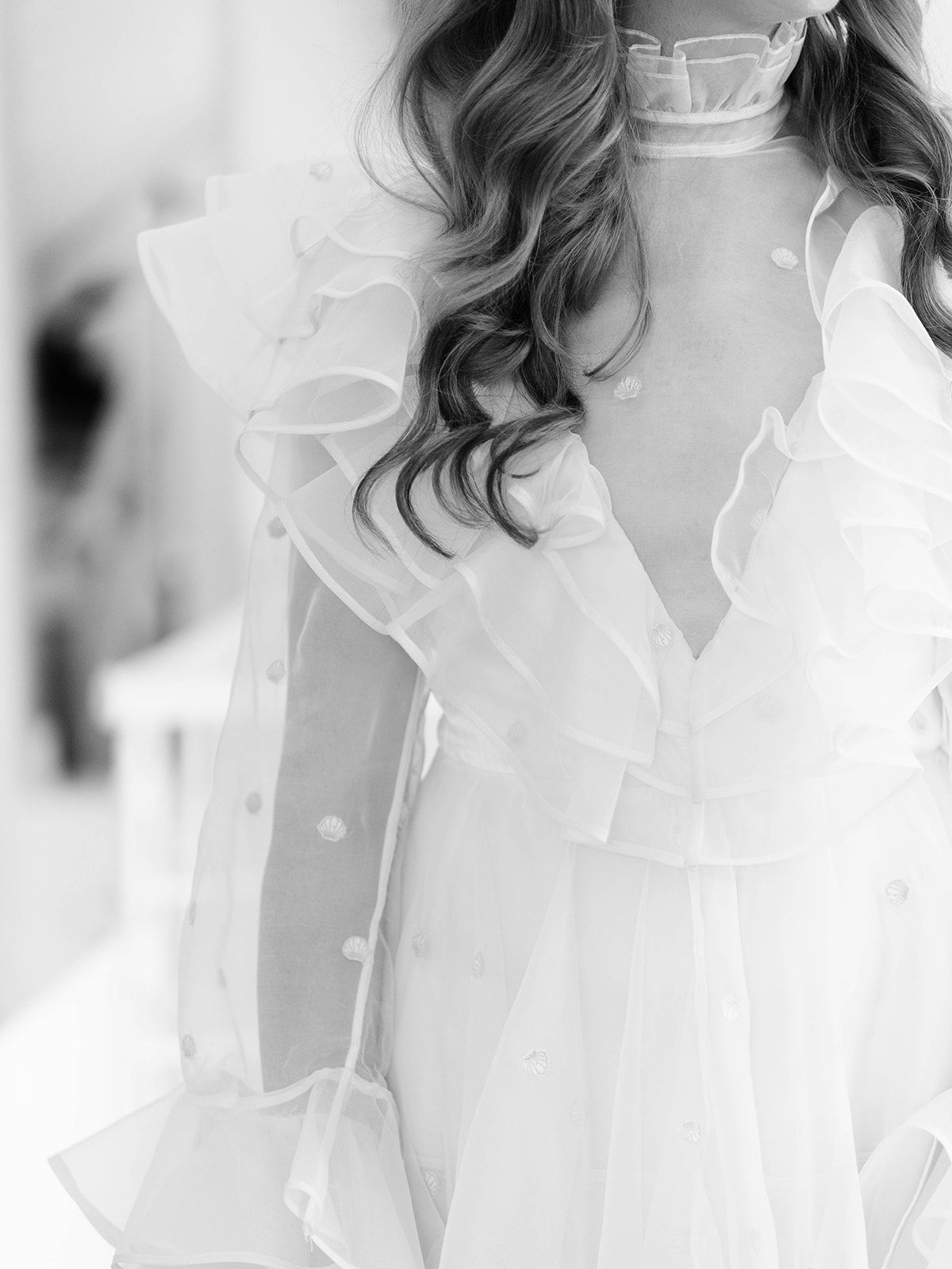 Black and white close-up of a delicate white ruffled wedding dress with sheer details.