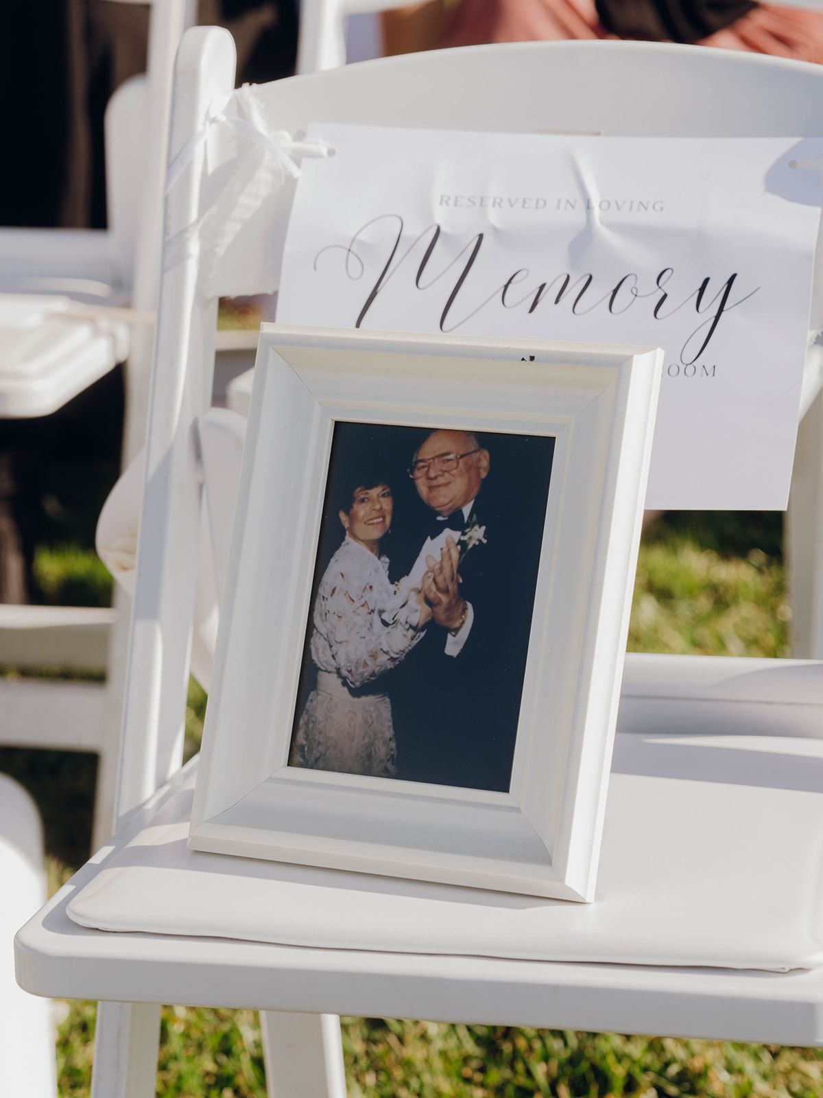 A framed photo displayed on a white chair with a 'Memory' sign during what appears to be an outdoor event.