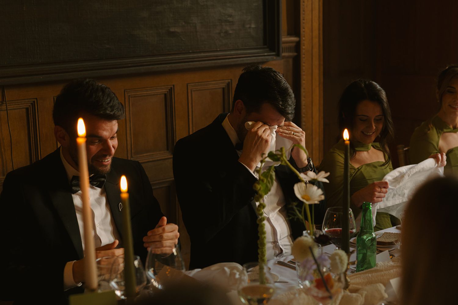 Candlelit wedding reception table with guests dining in an elegant indoor venue.