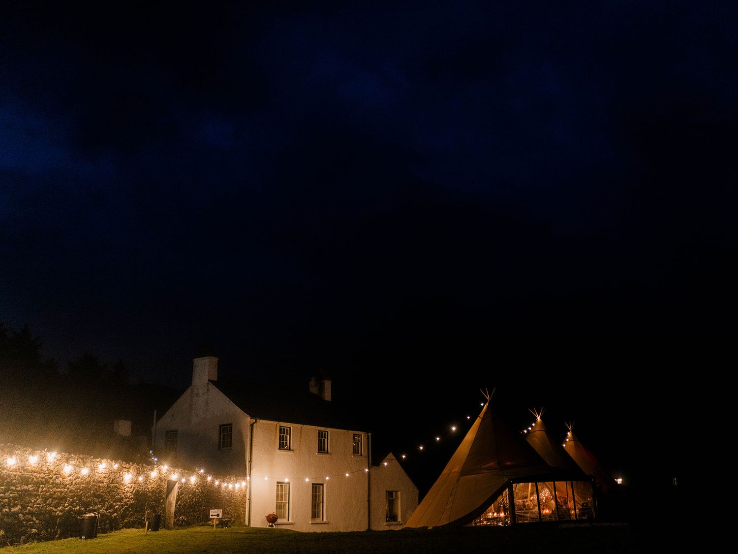 String lights illuminate white houses and tent structure against dark blue night sky.