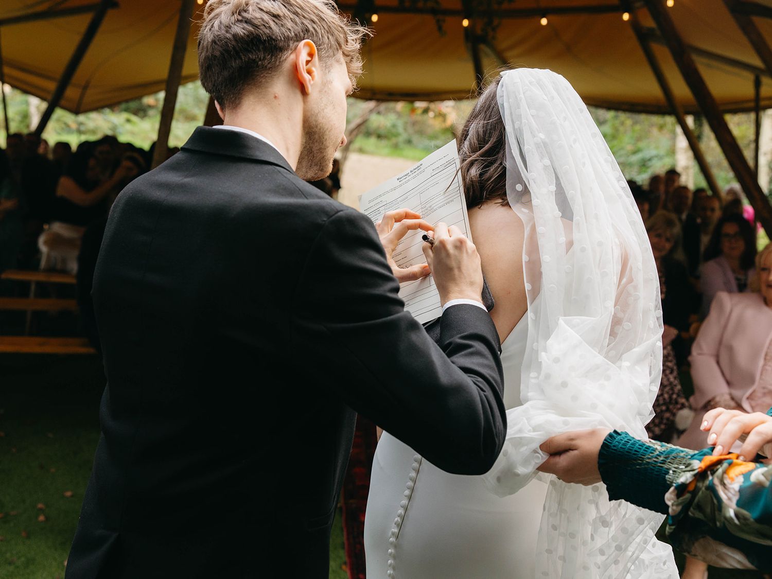 A wedding couple shares an intimate moment during their outdoor ceremony under a canopy with string lights.