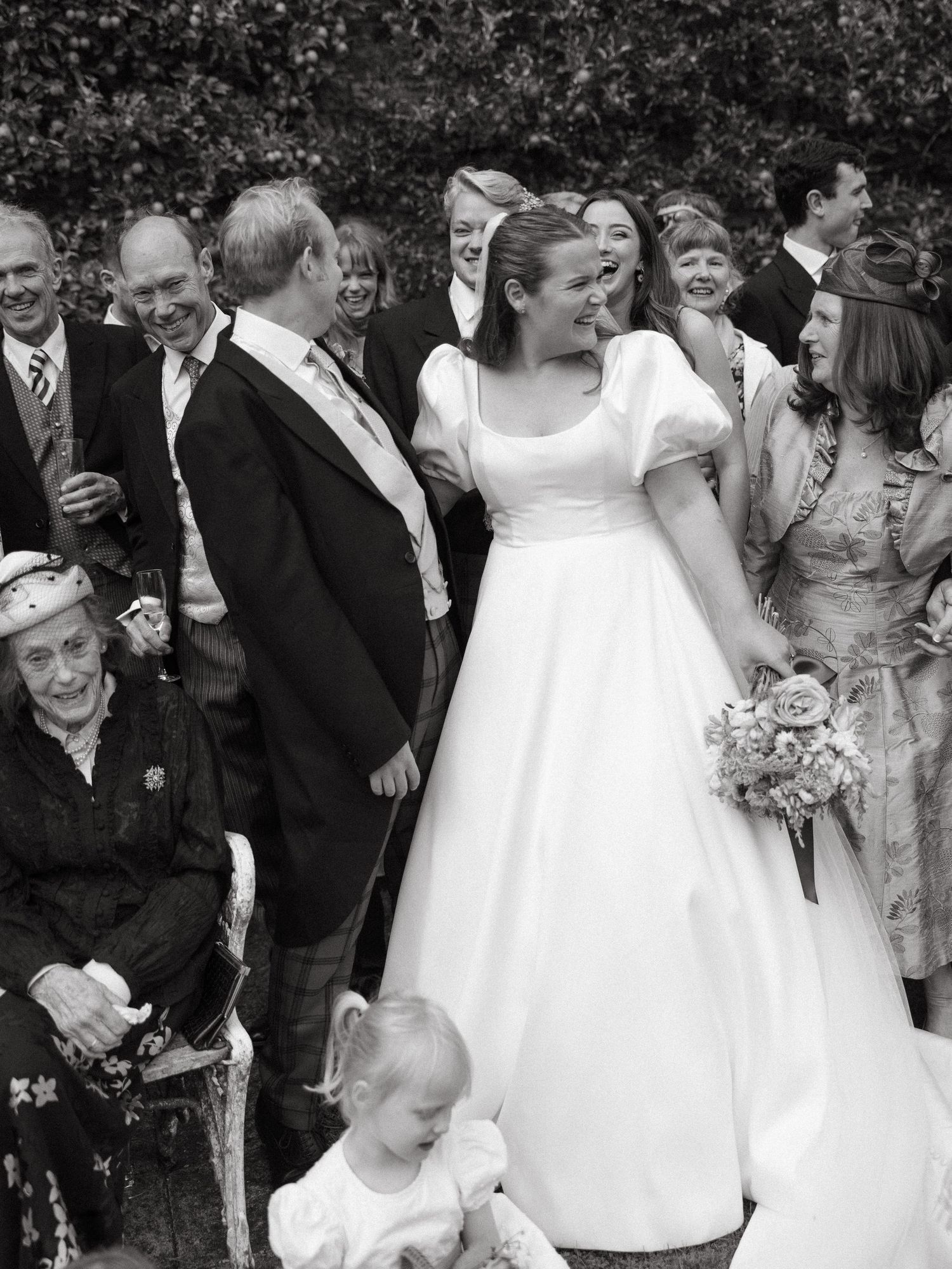 Wedding party and guests gather for a joyful group photo in black and white.