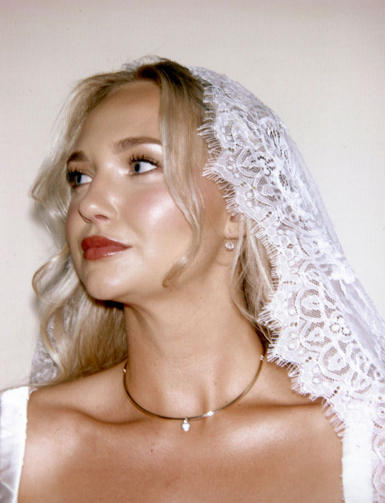 Blonde bride wearing a lace veil and pearl necklace, with elegant makeup and soft curls, gazing to the side.