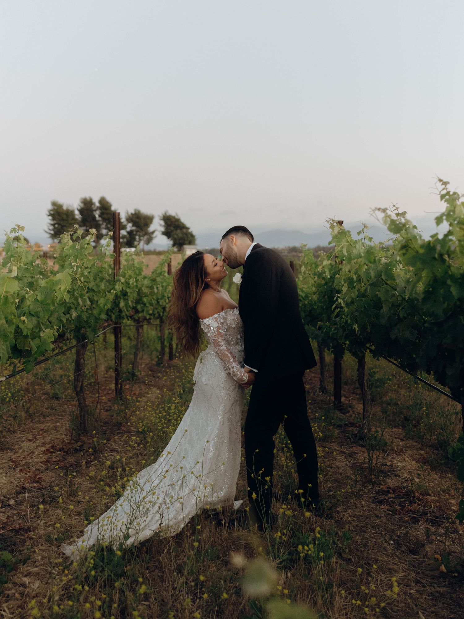 A couple shares a romantic moment among the grapevines at a scenic vineyard during sunset.