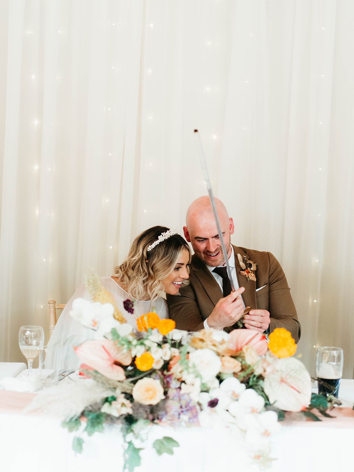 A bride and groom share a tender moment at their reception table decorated with colorful floral centerpieces.
