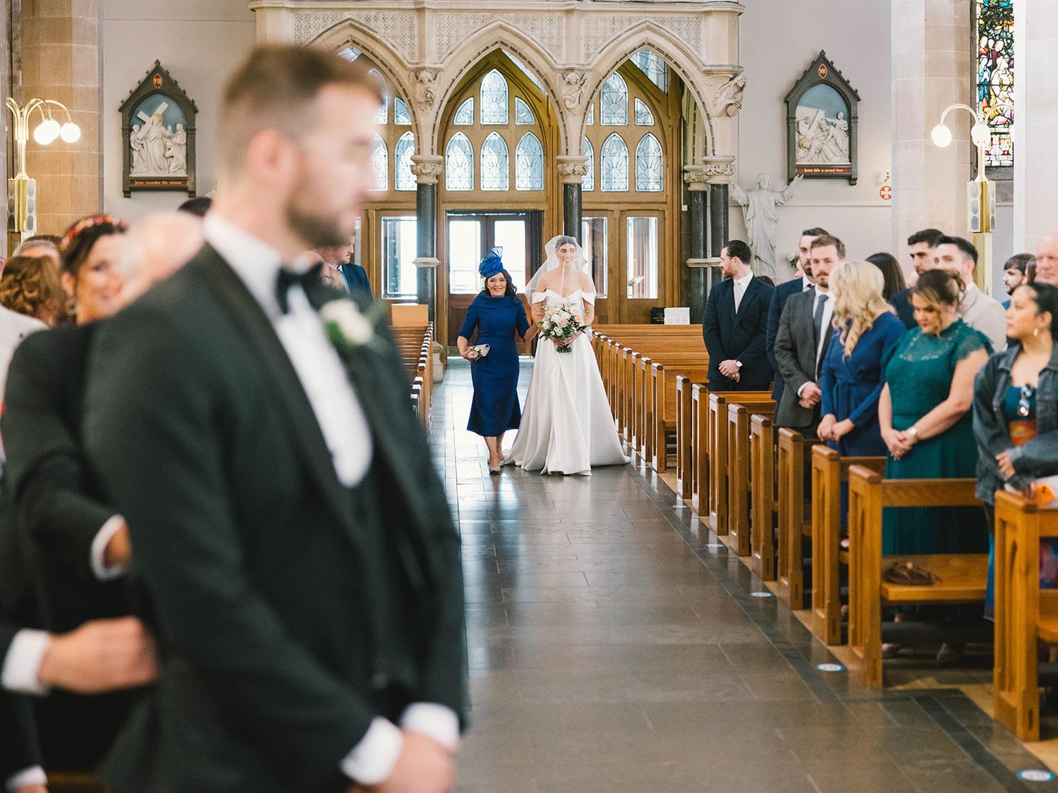 A traditional church wedding ceremony taking place in a beautiful gothic-style sanctuary with arched windows and wooden pews.