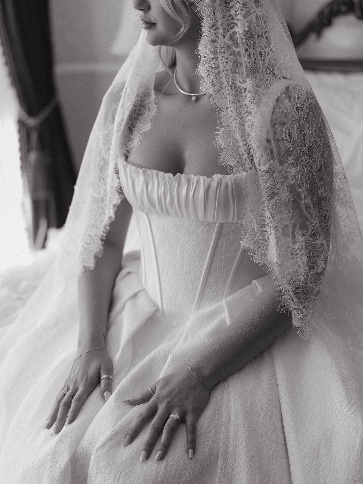 Elegant bride in a structured white corset gown with lace veil, captured in black and white photography.