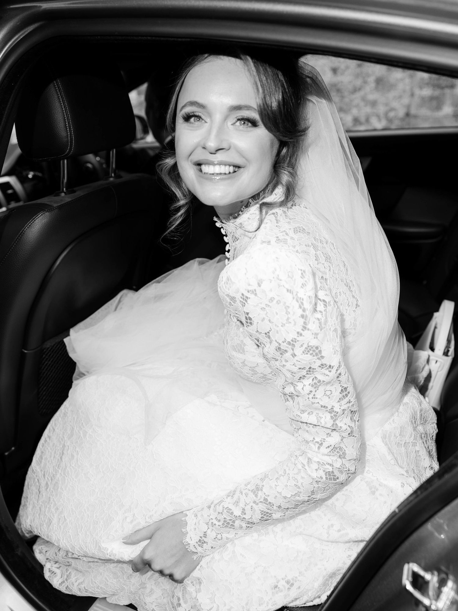 A bride in a white lace wedding dress sits in a car in a series of black and white photos.