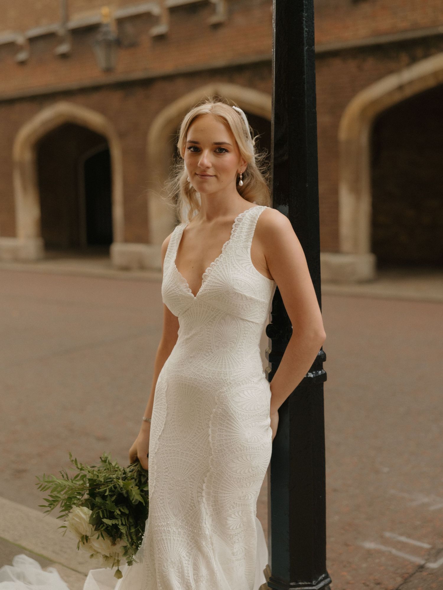 A bride in a white modern wedding dress poses by architectural columns with a simple bouquet in natural light.
