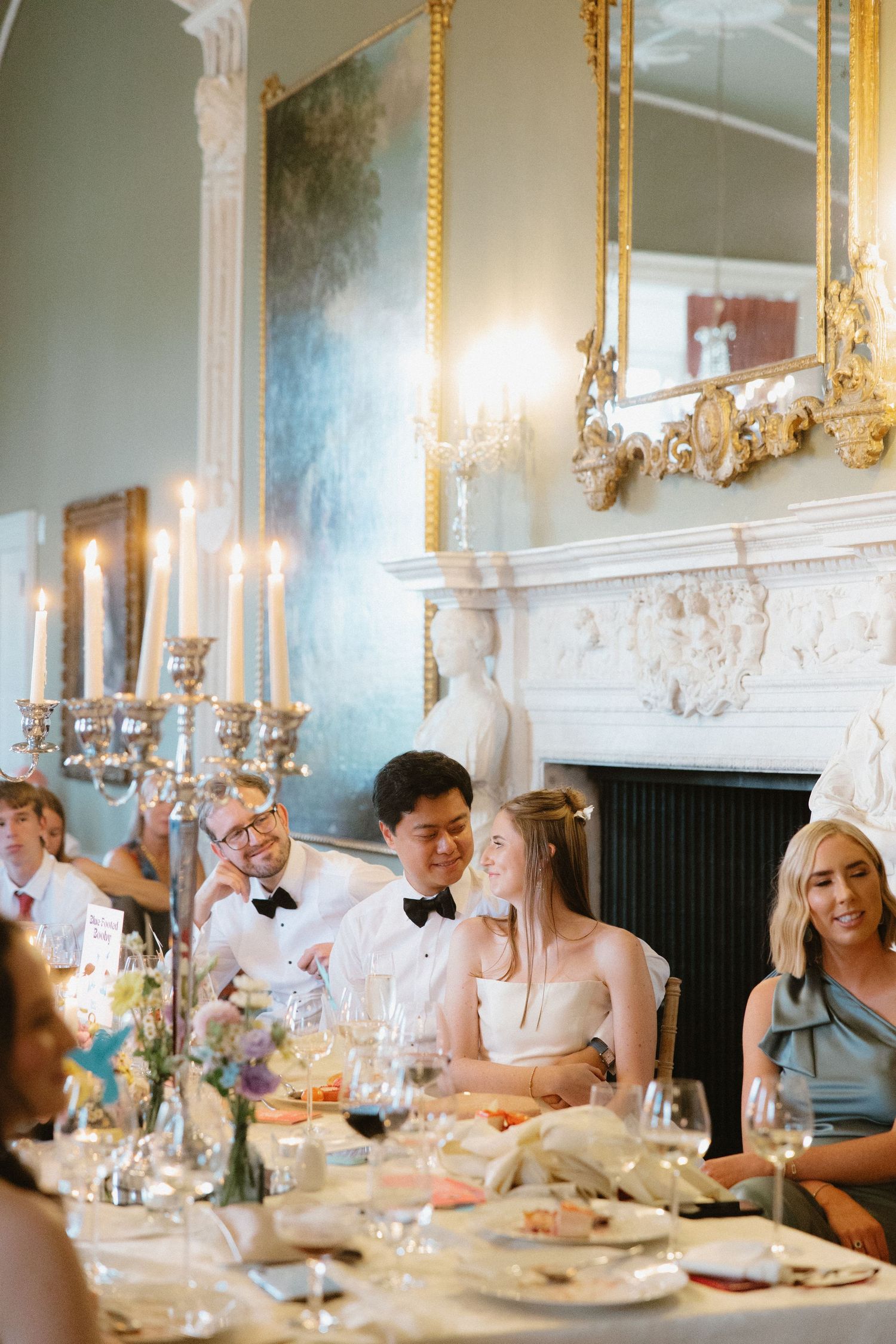 Elegant wedding reception dinner in an ornate room with candelabras and gold-framed mirrors.