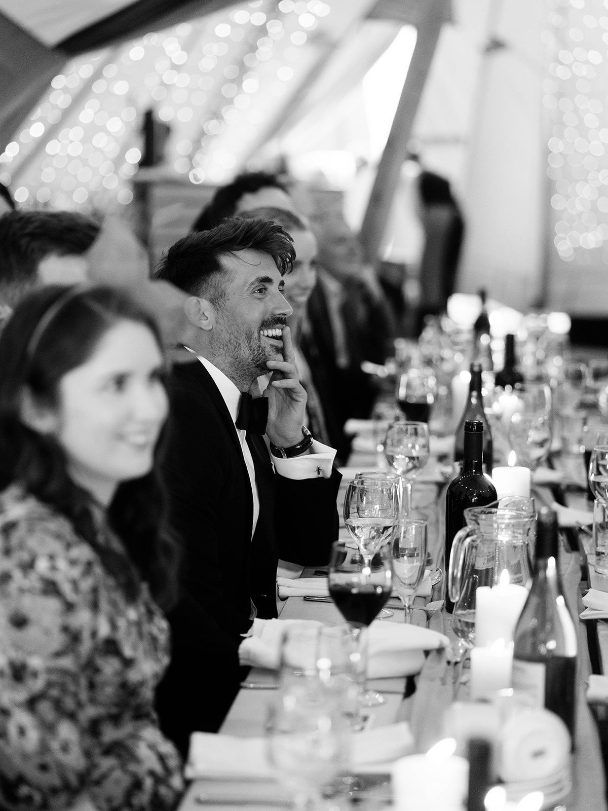 Black and white candid photo of guests laughing during wedding reception dinner.